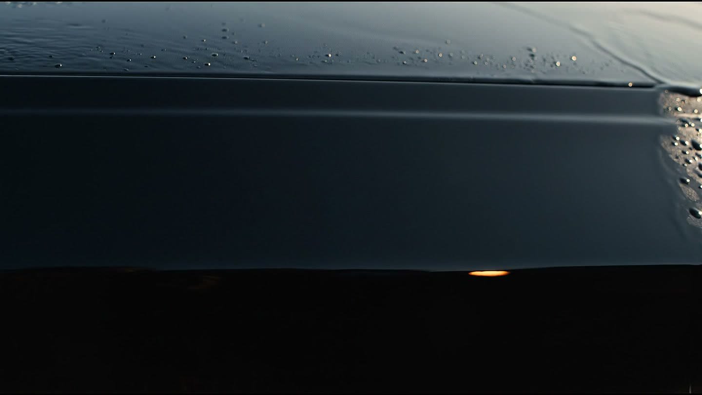 Black car paint washed clean, holding a reflection of the sun low on the water.
