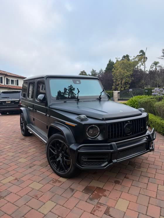 A finished black Mercedes G-Class on a brick paver driveway, paint reflecting the sky.